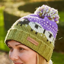 Pachamama Black Sheep Roll Back Bobble Beanie Purple. These Pachamama Black Sheep Bobble Beanies are knitted in Nepal by local villagers using local wools and natural dyes to UK designs. This beanie features a delightful black and white sheep pattern on a