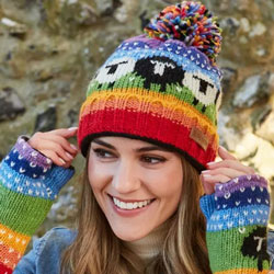 Pachamama Black Sheep Roll Back Bobble Beanie Rainbow. These Pachamama Rolled Bobble Beanies are knitted in Nepal by local villagers using local wools and natural dyes to UK designs. They feature a delightful black and white sheep pattern on a bright rain