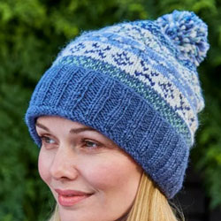 Pachamama Classic Fairisle Roll Back Bobble Beanie Denim. These Pachamama Bobble Beanies are knitted in Nepal by local villagers using local wools & natural dyes to UK designs. They feature a blue roll back in a ribbed design, with bands of patterned crea