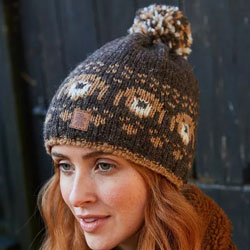 Pachamama Pooch Dog Bobble Beanie Bark. These Pachamama Bobble Beanies are knitted in Nepal by local villagers using local wools and natural dyes to UK designs. Each bobble beanie features a bark-brown background with a row of knitted pooch heads and a  f