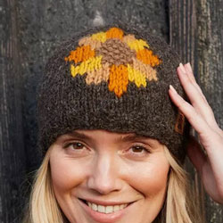 Pachamama Sunflower Beanie Hat. These Pachamama Beanies are knitted in Nepal by local villagers using local wools & natural dyes to UK designs. They feature a front facing sunflower design in orange, yellow & brown, set against a bark-brown beanie. The fo